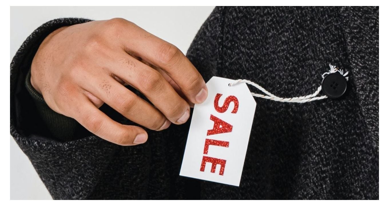 A hand holding a black friday sale hang tag hanged on a button of a coat.