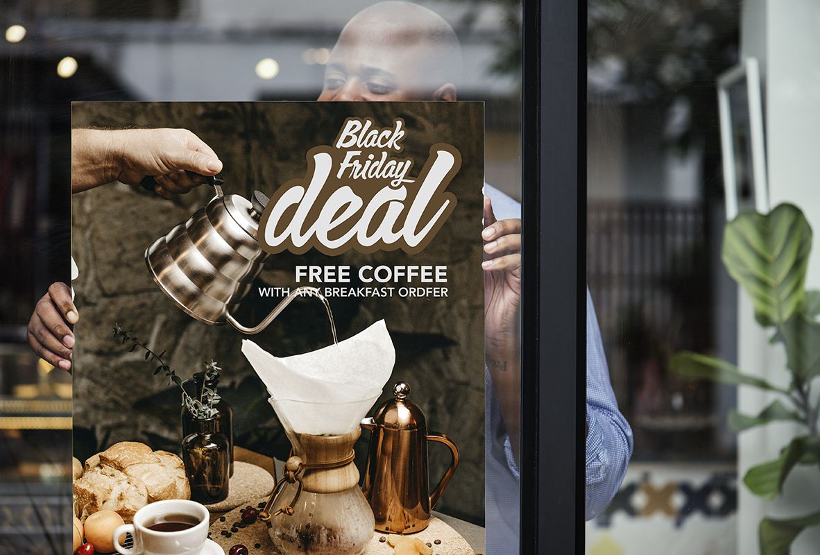 A man hanging a black friday discount poster on a shop window.