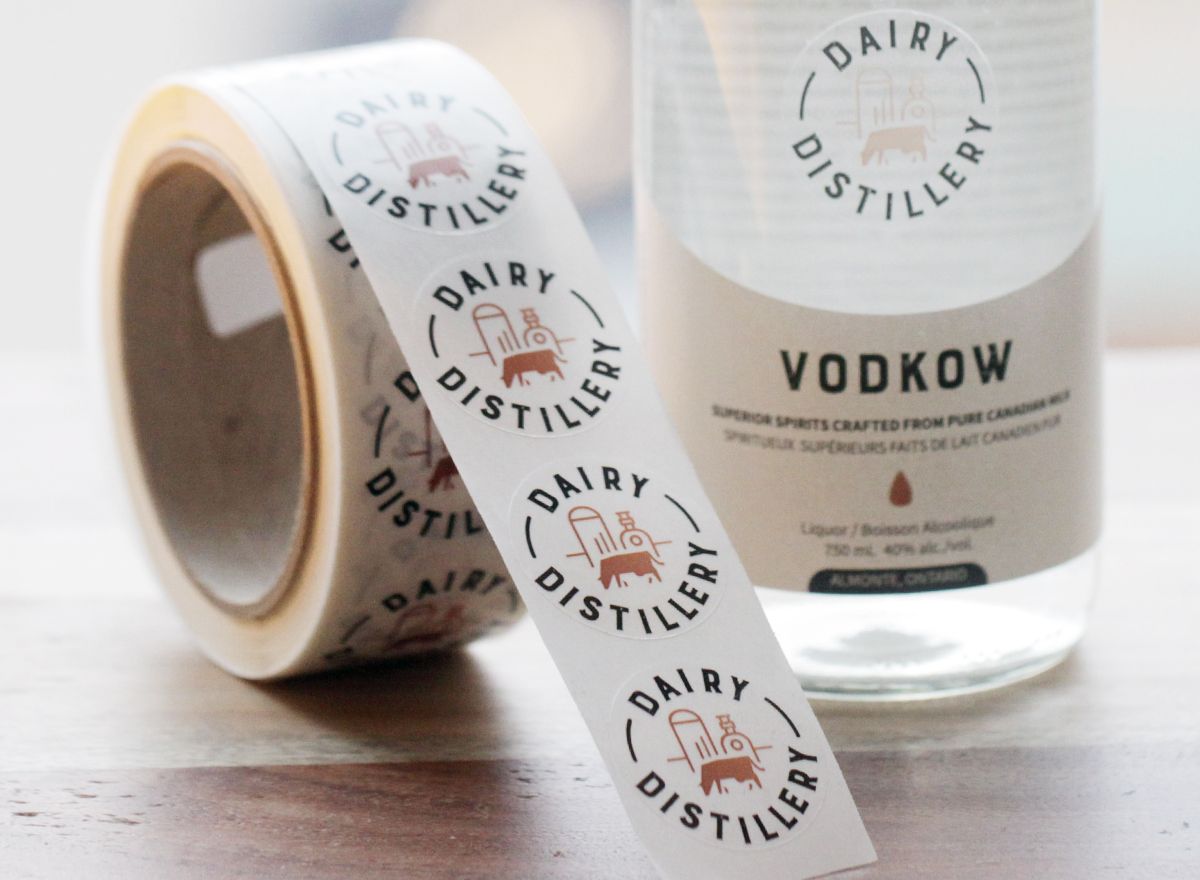 Custom labels printed on a roll next to a glass bottle with two different labels applied to the bottle.