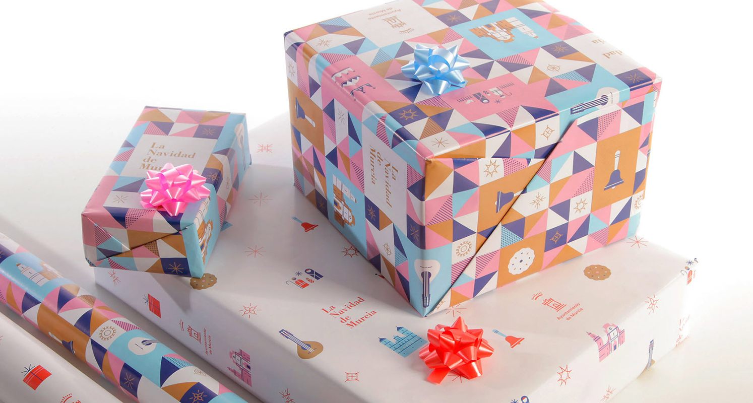 Holiday packaging, three wrapped boxes and two rolls of wrapping paper with holiday design.