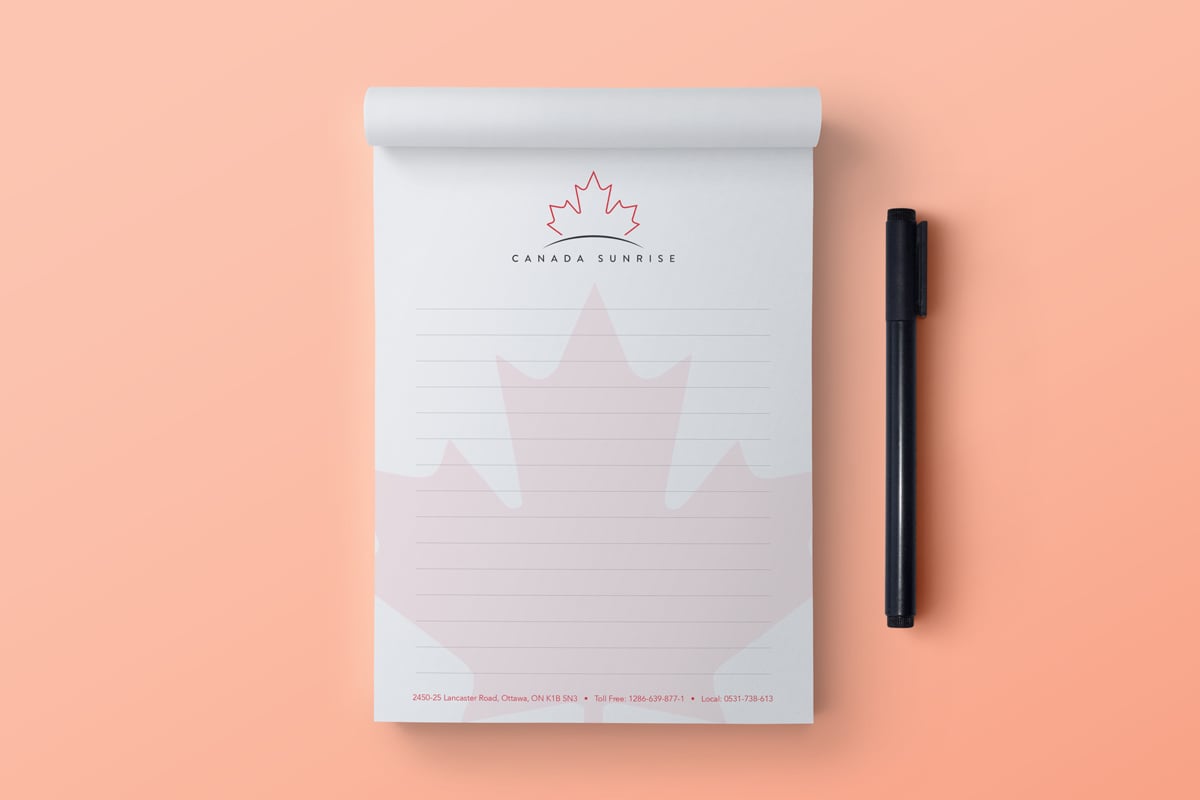 Image showing notepad with maple leaf design with a pen next to it on peach colored background.