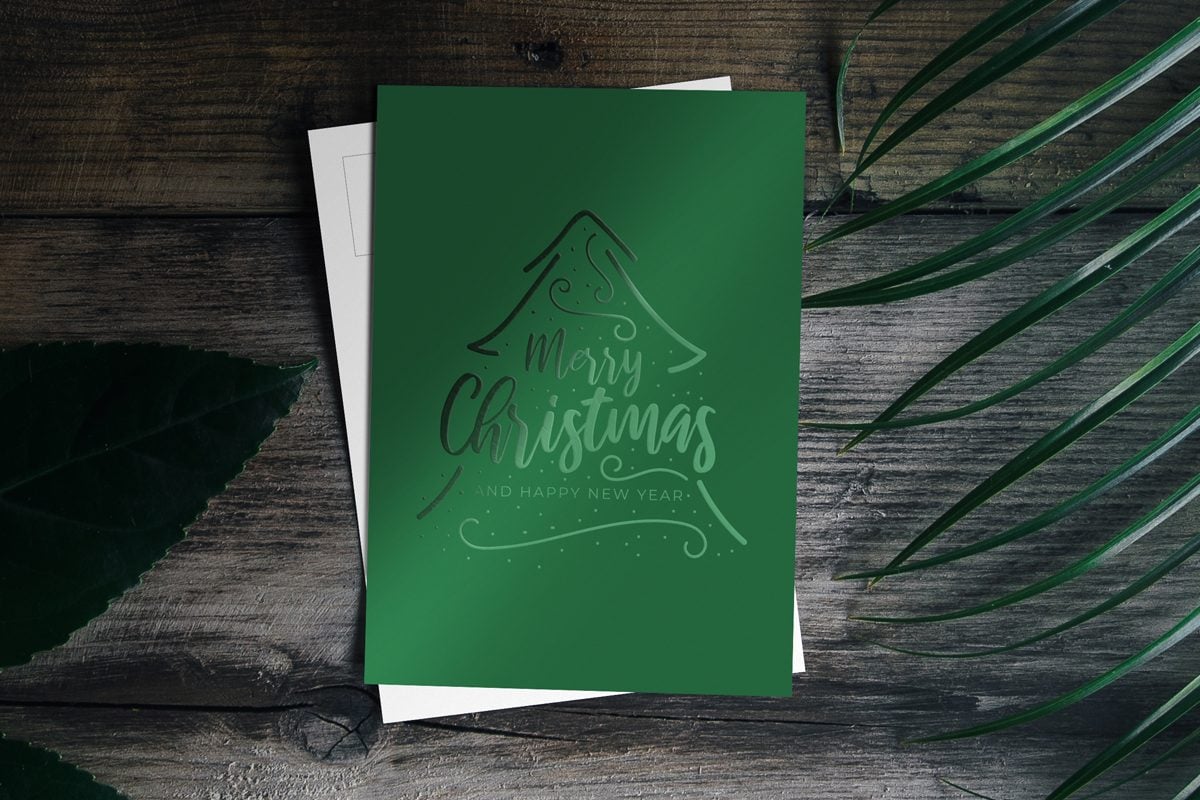 Image showing green Christmas postcard with green foiled Christmas tree on dark wooden surface.