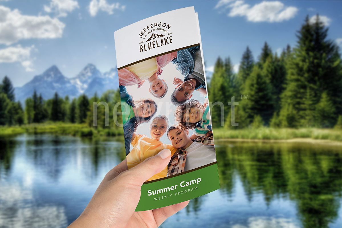 A hand holding summer camp brochure with lake in the background.