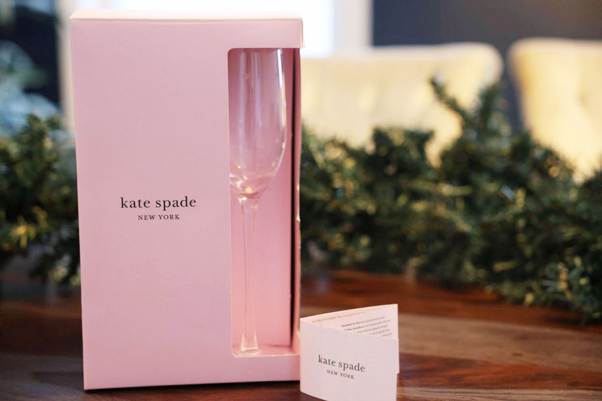 A pink packaging box printed with Pantone colors with a cutout on the side showing a champagne glass inside the box and a small folded hang tag next to the box, spot color vs CMYK.