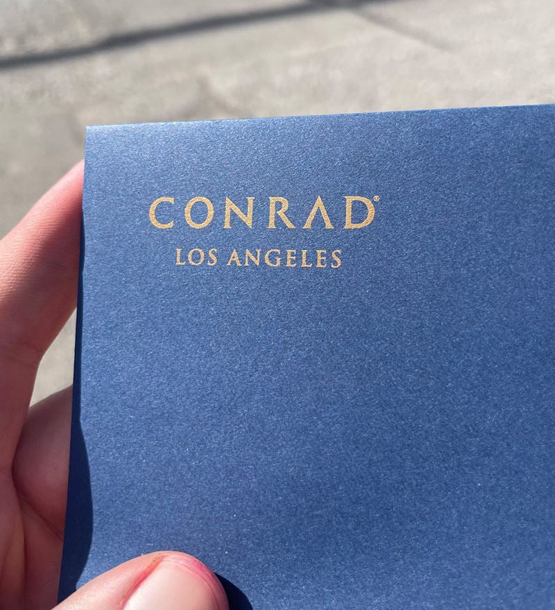A hand holding a blue envelope showing a printed logo in the top left corner, spot color vs CMYK.